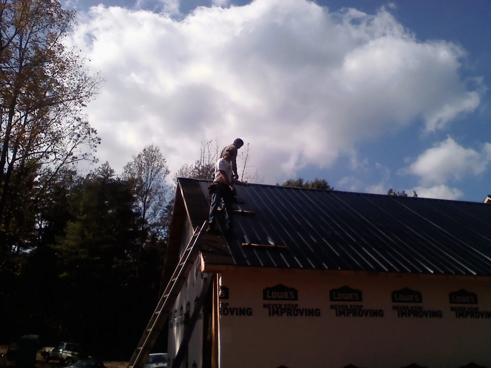 Roofer fastening dark metal panels high against a cloudy sky, from a Roof Inspection job in Lima